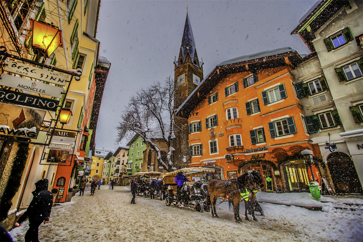 Schneefall in der Vorderstadt: Pferdeschlitten warten vor den erleuchteten Bürgerhäusern, dahinter der Kirchturm